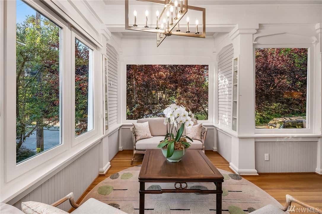 Elegant sunroom with hardwood flooring, comfortable chairs and large picture windows on all sides in an older remodelled house.