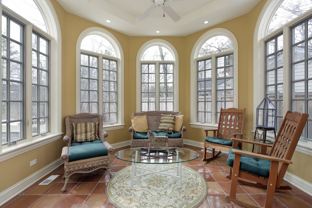 A tiled sunroom with a decorative rug, traditional chairs and a glass top table.