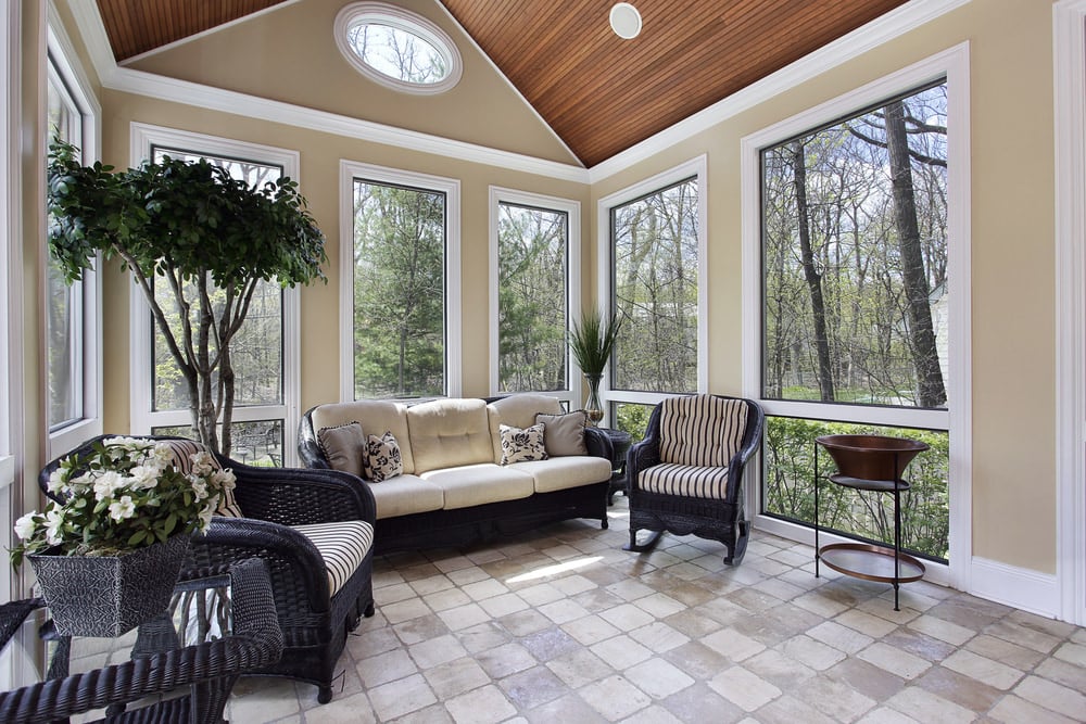 A country-style sunroom with tiled floor, glass windows and some potted plants.